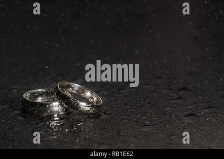 Silberne Hochzeit Ringe auf einem Rock Hintergrund mit Wassertropfen und Spray in der Luft Stockfoto