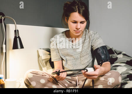 Das Thema hoher Blutdruck ist Bluthochdruck Krankheit. 22 Jahre alten jungen kaukasischen Frau verwendet eine automatische tonometer Druck zu Hause in t prüfen Stockfoto