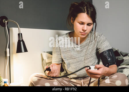 Das Thema hoher Blutdruck ist Bluthochdruck Krankheit. 22 Jahre alten jungen kaukasischen Frau verwendet eine automatische tonometer Druck zu Hause in t prüfen Stockfoto