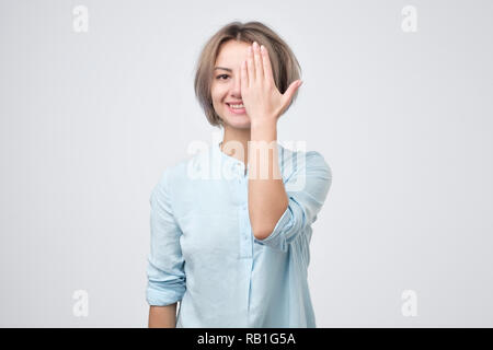 Europäische junge Frau im blauen Hemd ein Auge schließen mit der Hand und lächelt. Test Sehvermögen Gläser zu wählen. Stockfoto