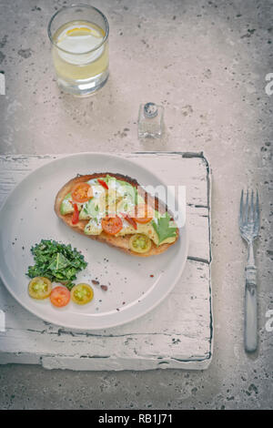 Geröstetes Brot mit Avocado und Tomaten serviert mit Grünkohl auf weiße Platte. Ansicht von oben Stockfoto