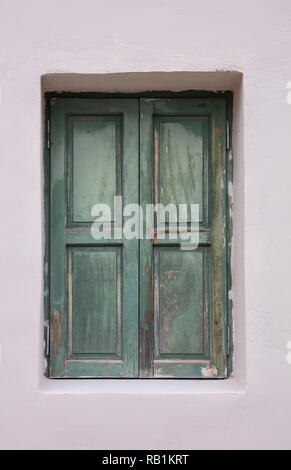 Altmodische getragen Fenster mit grünen Fensterläden aus Holz, geschlossen, auf bemalten Wand Hintergrund. Traditionelles Haus Fassade, Altstadt Plaka, Athens Griechenland Stockfoto