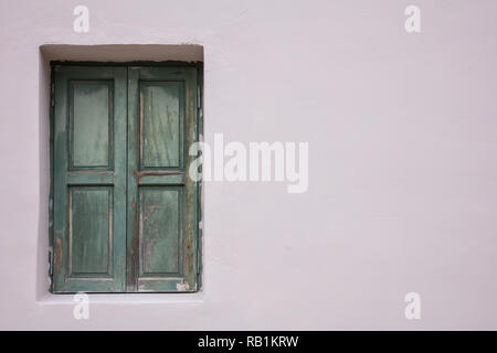 Altmodische getragen Fenster mit grünen Fensterläden aus Holz, geschlossen, auf bemalten Wand Hintergrund. Traditionelles Haus Fassade, Altstadt Plaka, Athens Griechenland Stockfoto