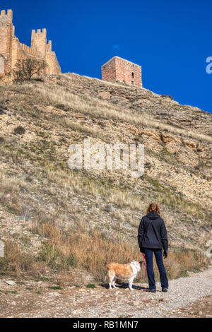 Eine vertikale Foto einer Frau in einer dunklen Jacke halten der Leine einer Blondine Border Collie an der alten Mauer aus Stein von Albarracin Spanien blickt auf ein Stockfoto