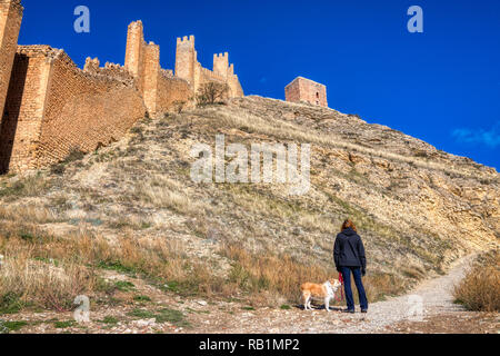 Eine horizontale Foto einer Frau in einer dunklen Jacke halten der Leine einer Blondine Border Collie an der alten Mauer aus Stein von Albarracin Spanien auf der Suche Stockfoto