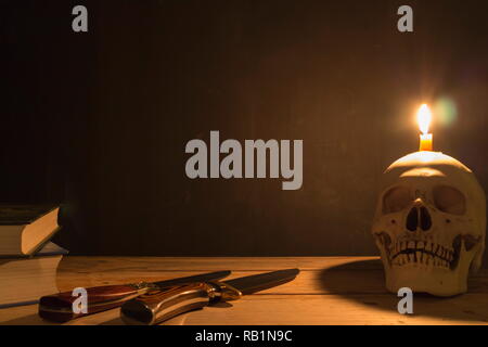 Menschlicher Schädel mit Kerzenlicht, Messer und Buch auf hölzernen Tisch in dem dunklen Hintergrund, Dekorieren für Halloween Theme mit kopieren. Stockfoto