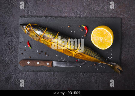 Geräucherte Makrele Fisch, Messer und Zitrone auf schwarzen Stein Schneidebrett. Stockfoto