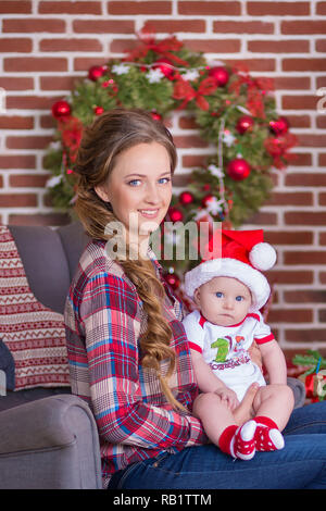 Mutter mit ein wenig Süßes und schöne Tochter verbringt Zeit spielt, coos, sitzen neben dem Weihnachtsbaum. Stockfoto