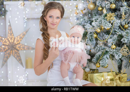 Mutter mit ein wenig Süßes und schöne Tochter verbringt Zeit spielt, coos, sitzen neben dem Weihnachtsbaum. Stockfoto