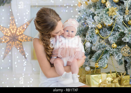 Mutter mit ein wenig Süßes und schöne Tochter verbringt Zeit spielt, coos, sitzen neben dem Weihnachtsbaum. Stockfoto