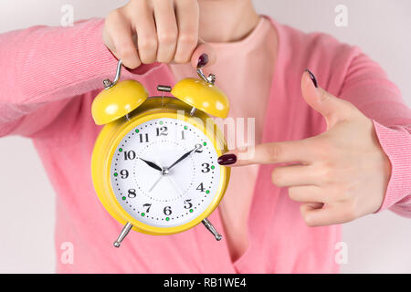 Junge Frau mit Retro alten Wecker in der Hand und zeigt mit dem Finger auf Zeit. Mädchen in rosa Pullover und Uhr ist Gelb. Konzept Bild Stockfoto