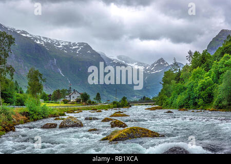 Eine Vogelperspektive über einen Fluss mit starken Stromfluss unter einem Wald und große Berge im Hintergrund in Norwegen Stockfoto