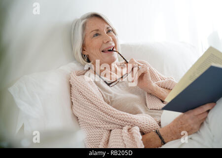Schöne ältere Frau im Bett lesen Stockfoto