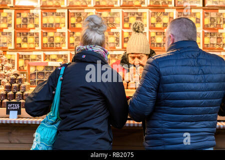 Menschen an Weihnachten Marktstand (potenzielle Kunden), die vom Händler serviert, kaufen Schokolade (Schokolade teacakes in Kästchen angezeigt) - York, England, Großbritannien Stockfoto