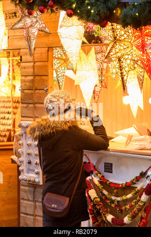 Frau an Weihnachten Marktstand (potenzielle Kunden) auf Papier Sterne leuchten (Laternen) auf dem Display, Gießen warmen goldenen Glühen - York, England, UK. Stockfoto