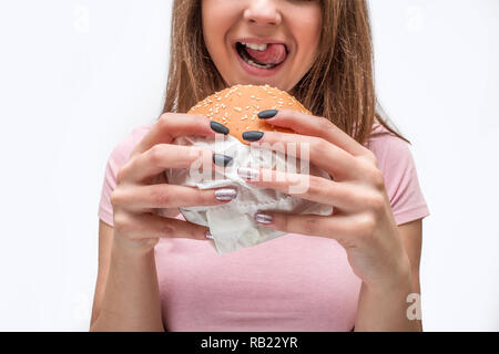 Schnittansicht des jungen Mannes holding Burger in der Hand. Sie lecken Lippen mit der Zunge. Auf weissem Hintergrund. Stockfoto