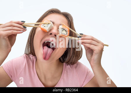 Verspielte junge Frau, die Stücke von Sushi vor den Augen und Zunge. Auf weissem Hintergrund. Stockfoto