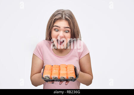 Junge Frau Blick auf Satz von frischem Sushi aufgeregt. Sie halten es in den Händen. Auf grauem Hintergrund. Stockfoto