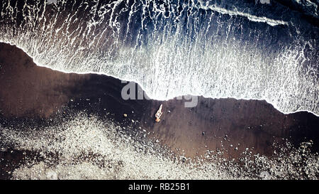 Junge entspannt kaukasischen Dame legt am Strand am schwarzen vulkanischen Sand, Sonne und wartet auf den großen Wellen - Urlaub und Reisen t zu trocknen Stockfoto