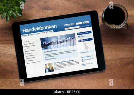 Die Website von Handelsbanken ist auf einem iPad Tablet gesehen, auf einer hölzernen Tisch zusammen mit einem Espresso und einem Haus Anlage (nur redaktionelle Nutzung). Stockfoto