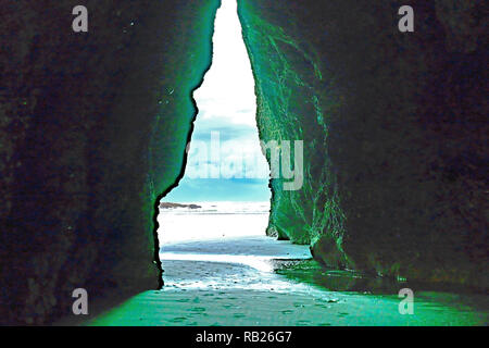 Tageslicht Streiks Wand markieren grünen Algenwachstum im Blick durch Torbogen Felsen zu dramatischen Himmel und Meer an Puponga South Island, Neuseeland. Stockfoto