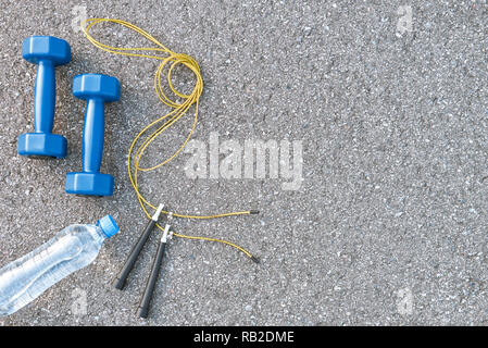 Die beste Kombination, um Gewicht zu verlieren. Seil springen, eine Flasche Wasser und zwei blauen leichten Hanteln bei Asphalt liegen Stockfoto