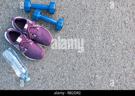 Motiviert zum Training. Zwei blaue dumpbells und eine Flasche Wasser liegen in der Nähe von Purple Sport Schuhe Stockfoto