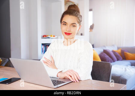 Der schöne junge Frau mit ihrem Laptop während am Schreibtisch sitzen und Lernen zu Hause. Stockfoto