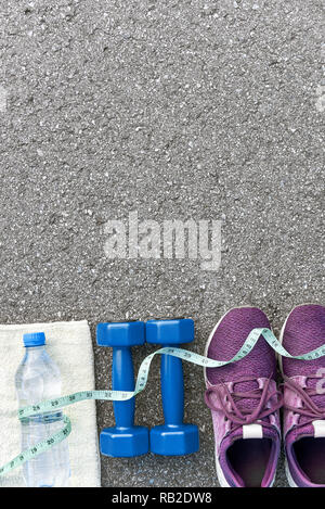 Motiviert zum Training. Zwei blaue dumpbells und eine Flasche Wasser liegen in der Nähe von Purple Sport Schuhe. Flasche, das auf weißem Handtuch, Maßband Abdeckungen Stockfoto