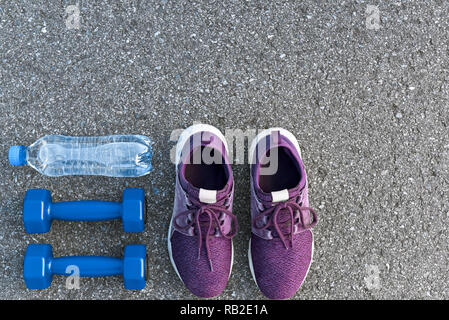 Motiviert zum Training. Zwei blaue dumpbells und eine Flasche Wasser liegen in der Nähe von Purple Sport Schuhe Stockfoto