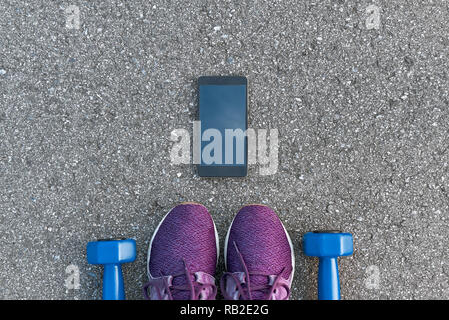 Smart sport Gadgets. Foto von dumpbells und lila Turnschuhe am Asphalt Hintergrund abgeschnitten. Sport motivation mobile Apps Stockfoto