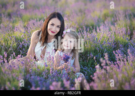 Junge schöne Frau Mutter mit reizenden Tochter zu Fuß auf der Lavendel Feld an einem Tag am Wochenende im wunderschönen Kleider und Hüte Stockfoto