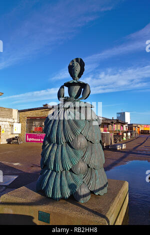 Die Shell Lady Bronze Zustand mit der Pier hinter ihr auf einem blauen Himmel sonnigen Tag Stockfoto