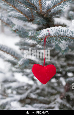 Zwei rote Herzen hängende Textilien an verschneiten Tannen-Zweig, Weihnachten und Valentinstag gruss Konzept, getönt Stockfoto