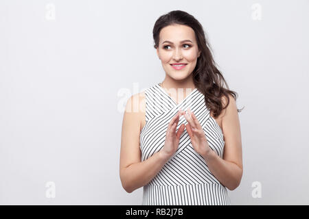 Portrait von toothy smiley Schöne junge brünette Frau mit Make-up und gestreiften Kleid Stehen und weg schauen mit gerissen. indoor Studio shot Stockfoto