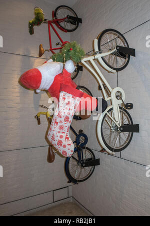 Weihnachtsmann Santa Claus auf einem Fahrrad fahren, eine Wand mit zwei anderen Bikes Stockfoto
