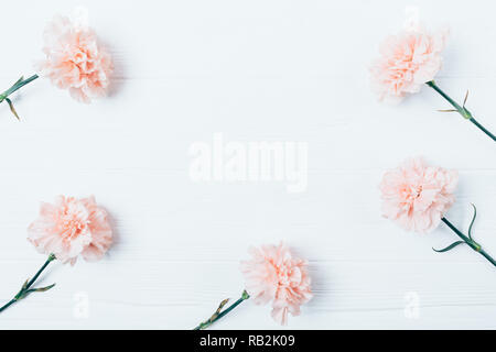 Dekorative Rahmen von rosa Nelken auf weißem Holz- Hintergrund mit leeren Raum in der Mitte, flach. Stockfoto