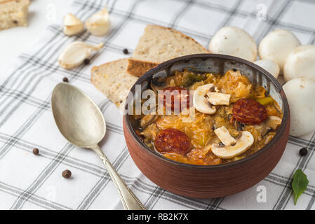 Slowakische Weihnachten nationalen Kohlsuppe in kleinen schwarzen Topf mit Wurst auf der Tischdecke Hintergrund. Stockfoto