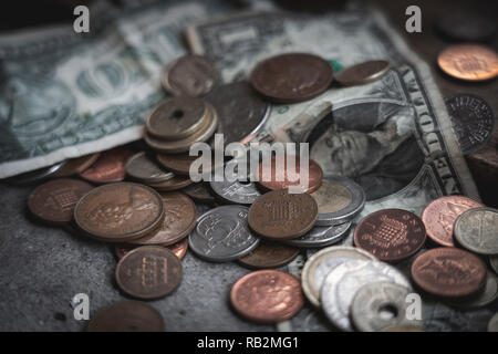 Münzen und Dollarscheine auf konkrete Tisch verstreut. Geld und Wirtschaft Konzept. Stockfoto