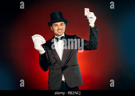 Berufliche Tätigkeit. Magier, Handschuhe und Hut stehen isoliert auf Wand Tricks mit Karten zeigen freudigen Lächeln Stockfoto