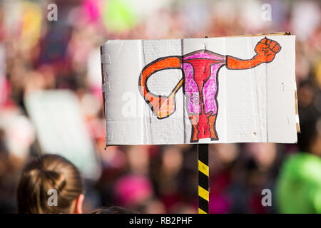 Eine Hand gezeichnet Zeichen, die die reproduktive Organe bilden eine Faust über die Masse während des März 2018 Demonstration der Frauen steigt. Stockfoto