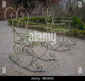 Schaukelstühle aus Metall, das in der ummauerten Garten hinter den Cottages neben den Ruinen der Cowdray Haus, Midhurst, West Sussex, Großbritannien Stockfoto