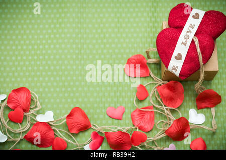 Valentinstag. Ein rotes Herz mit einem alten Thread zu einer Geschenkbox gebunden liegt auf einem grünen Polka Dot Hintergrund. Valentinstag. Herz Anhänger. Platz für Text. Stockfoto