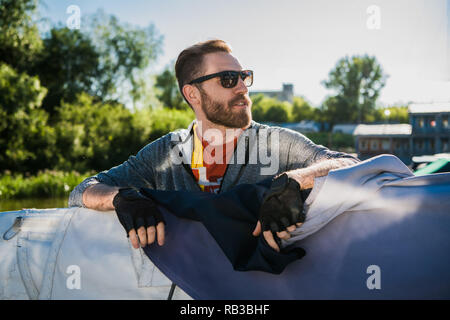 Stattlicher Mann mit der Yacht zu reisen. Casual Outfit, Mann in Grau hoodie gekleidet, Frühling, bärtigen Mann mit Sonnenbrille auf dem Boot. Stockfoto