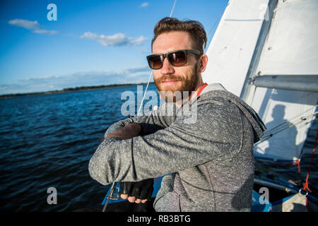 Ein Mann mit Sonnenbrille und legere Kleidung, als er ein kleines Beiboot rund um einen See oder Fluss Laufwerke Stockfoto