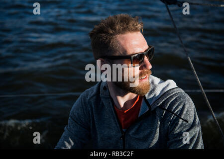 Close up Portrait bärtiger Mann Modell mit Sonnenbrille und Kapuze schaut weg, den Sonnenuntergang im Meer. Stockfoto