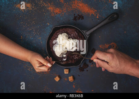 Brownie mit Schokolade und Sahne Vanilleeis in einer Pfanne über blauen Hintergrund. Blick von oben. Stockfoto