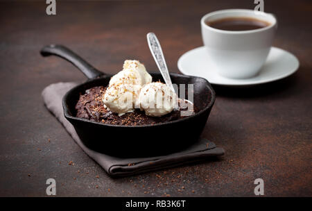 Brownies mit Vanilleeis in einer Pfanne, eine Tasse Kaffee auf braunem Hintergrund Stockfoto