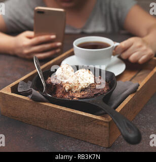 Brownies mit Vanilleeis in einer Pfanne, eine Tasse Kaffee auf braunem Hintergrund Stockfoto