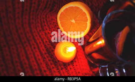 Glühwein im Glas Becher, brennende Kerze auf einem dunklen roten Hintergrund. Red Hot Wein Stockfoto